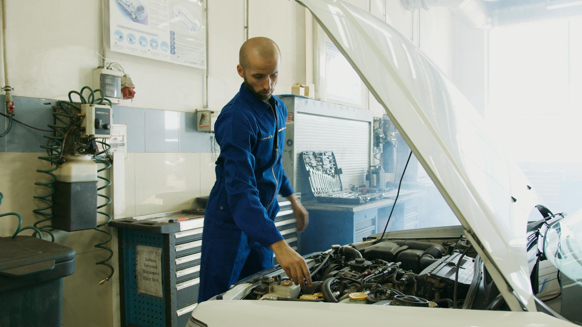 Mechanik w niebieskim kombinezonie ogląda silnik auta w warsztacie