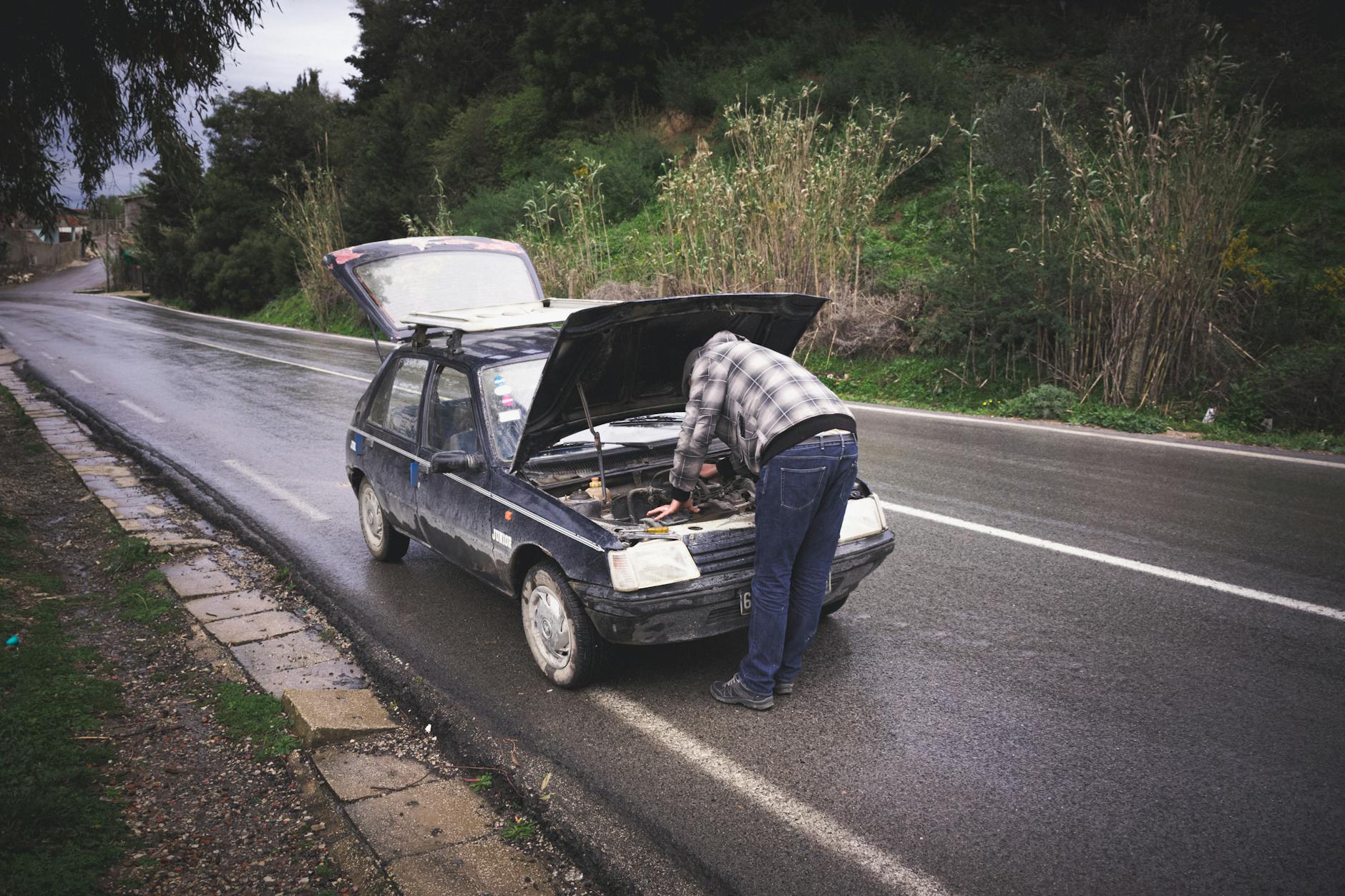 Kierowca naprawia auto na deszczowej drodze podczas awarii na trasie